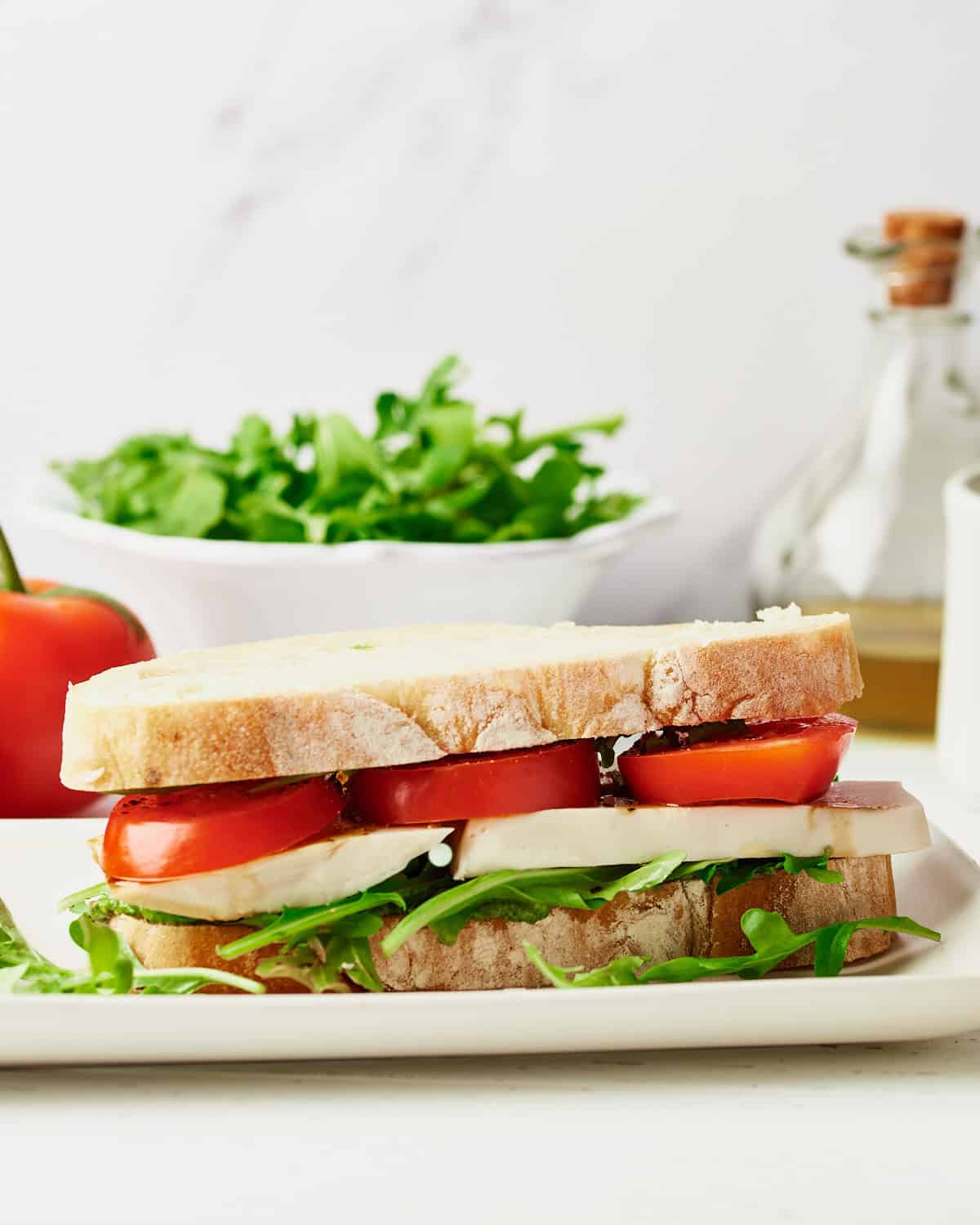 One vegan Caprese Sandwich on a white platter with arugula leaves.
