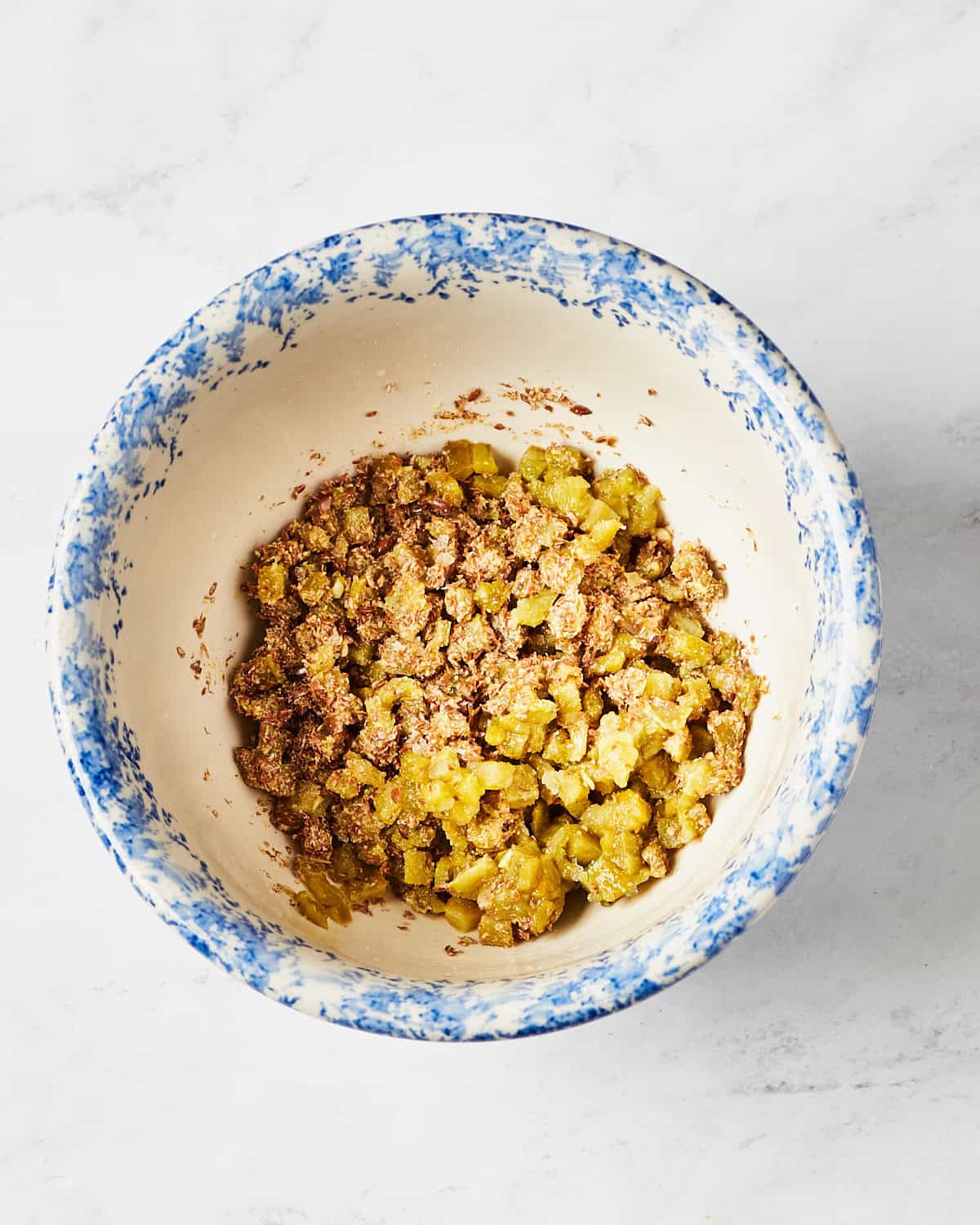 Roasted green chile mixed with flaxseed meal in a bowl on a marble surface.