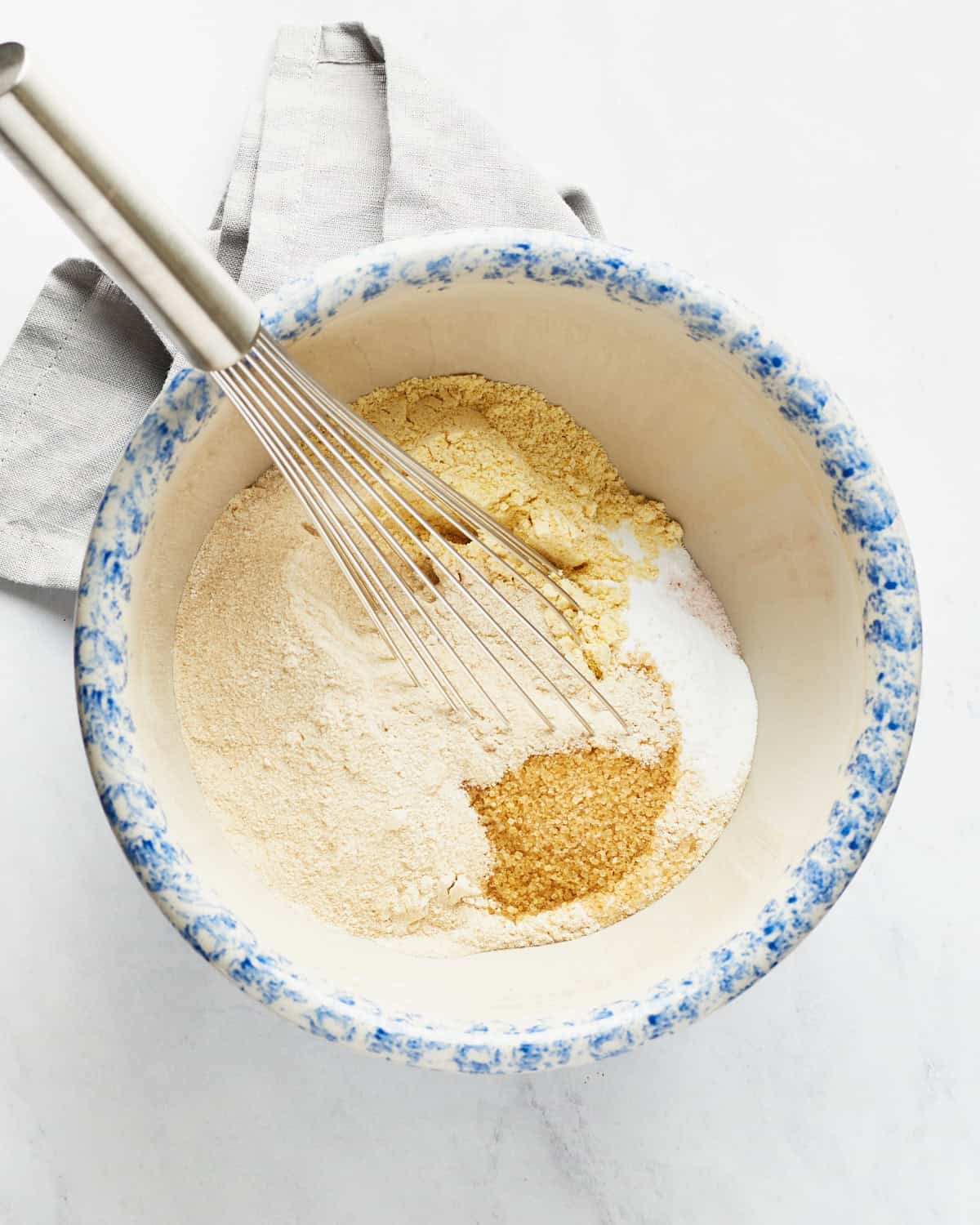 Dry ingredients with a whisk in a large bowl with a napkin on a marble background.