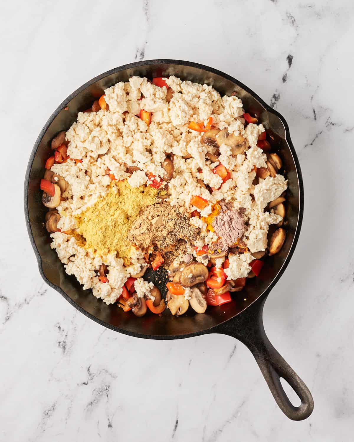Cooking vegetables with the tofu and seasoning added to a cast iron skillet.