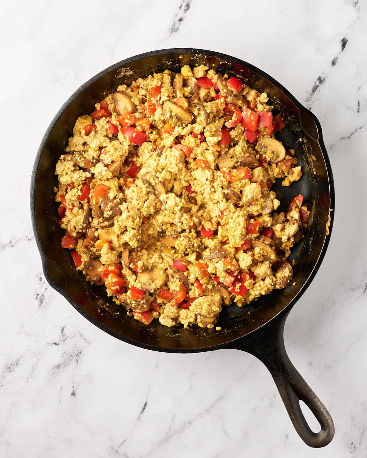 Tofu scramble with red bell pepper and seasonings in a cast iron pan.
