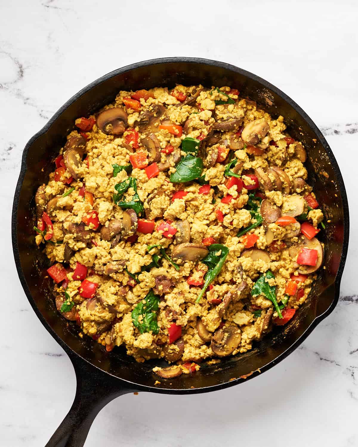 Cooked vegan mushroom tofu scramble with spinach and mushroom in a cast iron skillet.