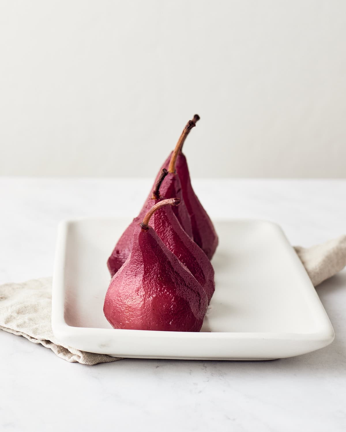 Four poached pears in red wine on a white platter.