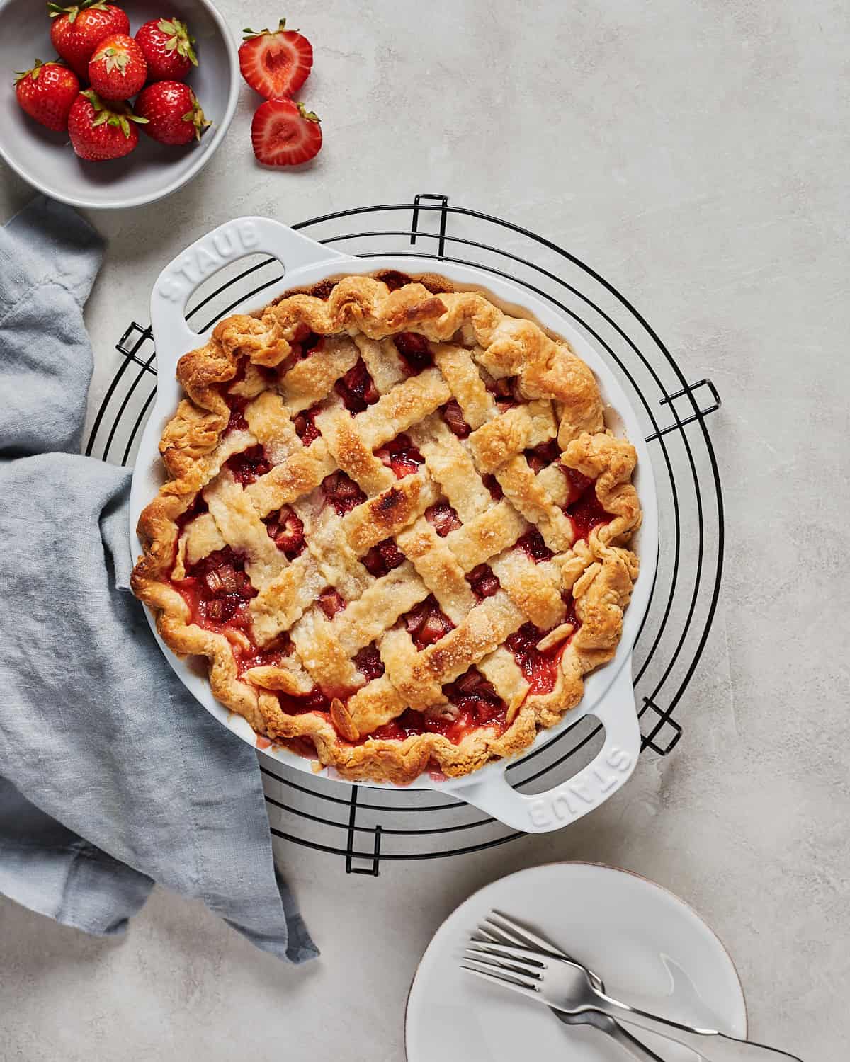 Vegan Strawberry Rhubarb Pie on a cooling rack with plate and forks.
