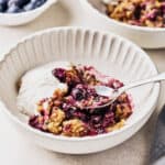 A bowl of vegan blueberry cobbler, close up with a spoon in it with a side of vegan ice cream.