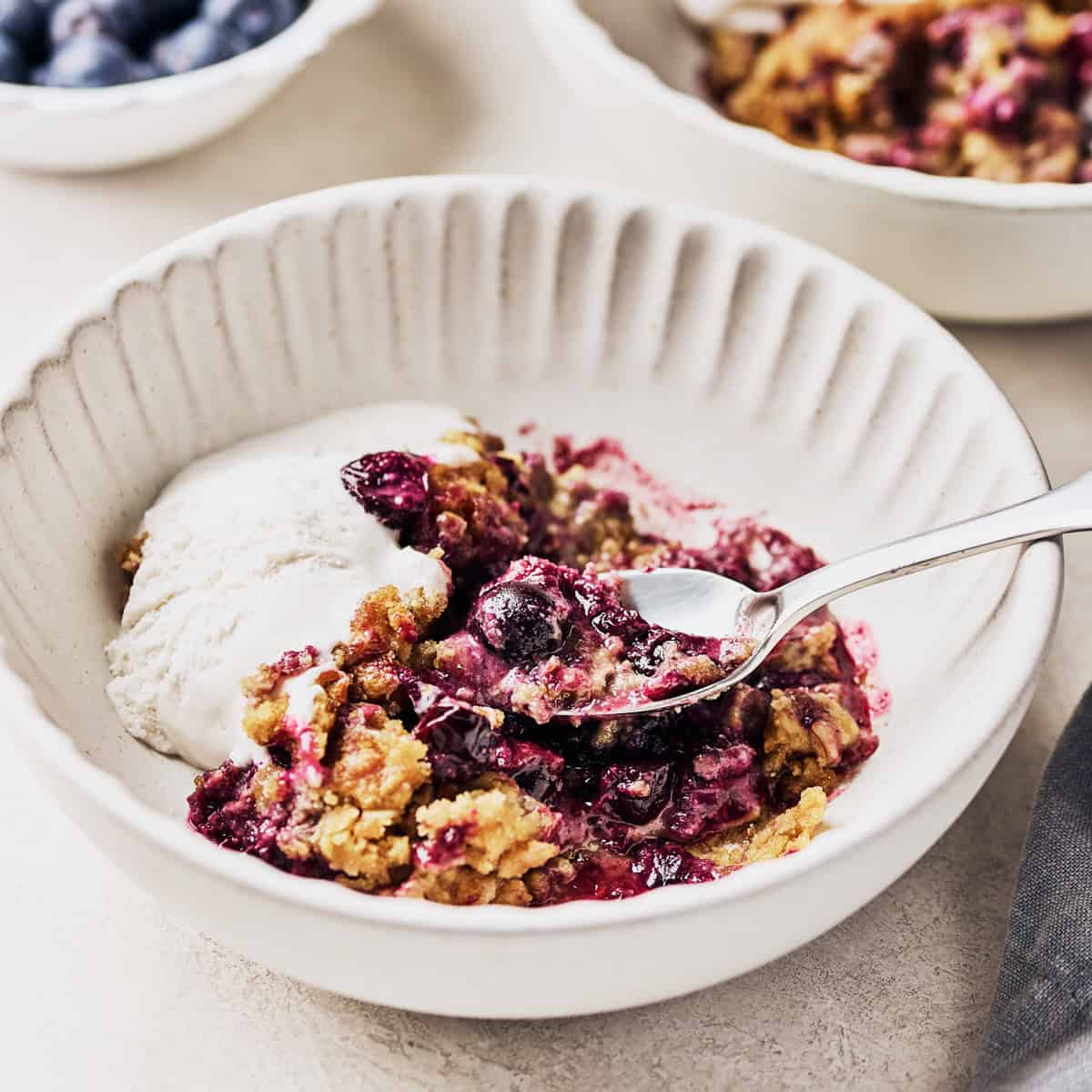 A bowl of vegan blueberry cobbler, close up with a spoon in it with a side of vegan ice cream.