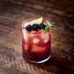 Blackberry Bourbon Smash cocktail garnished with mint and lime on a wooden surface.