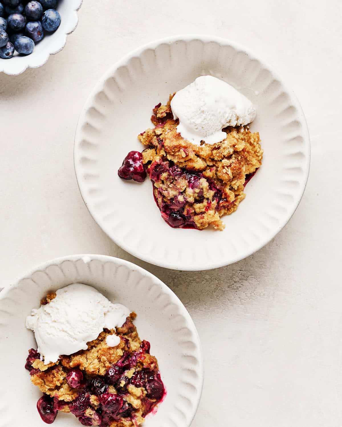 Two servings of vegan blueberry cobbler in bowls with whipped coconut cream.