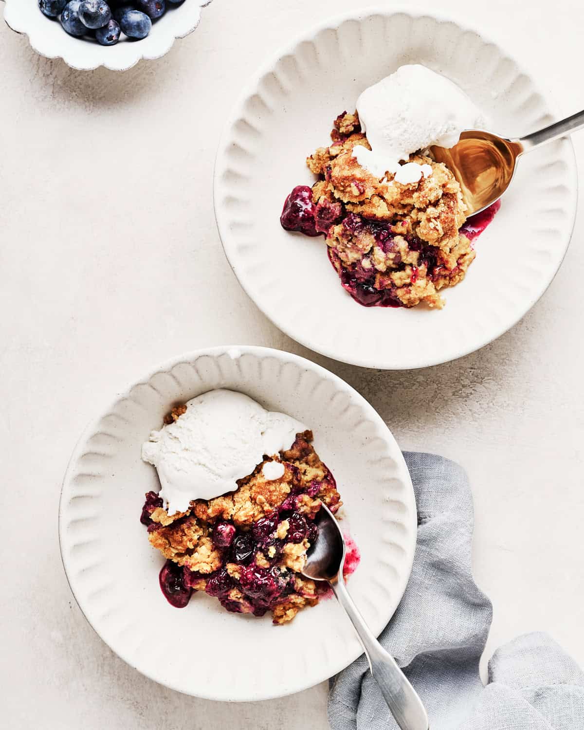Two servings of vegan blueberry cobbler in bowls with whipped coconut cream.