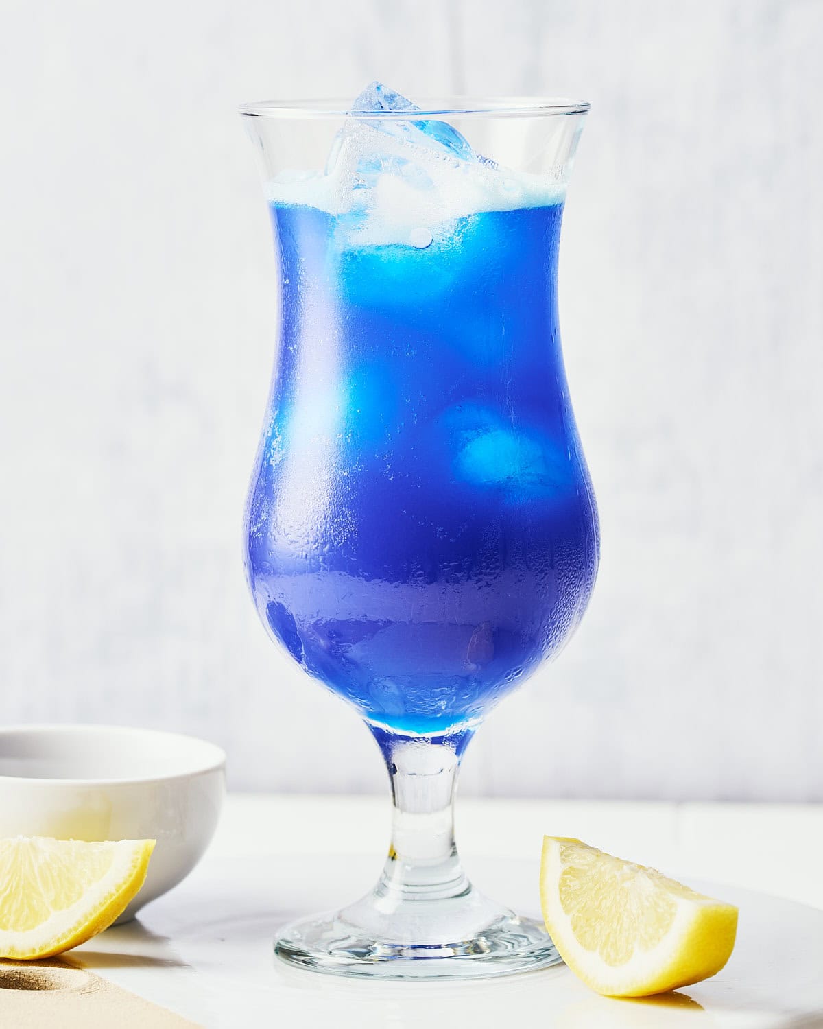 Adding club soda to make Blue Lagoon Mocktail in a hurricane glass.