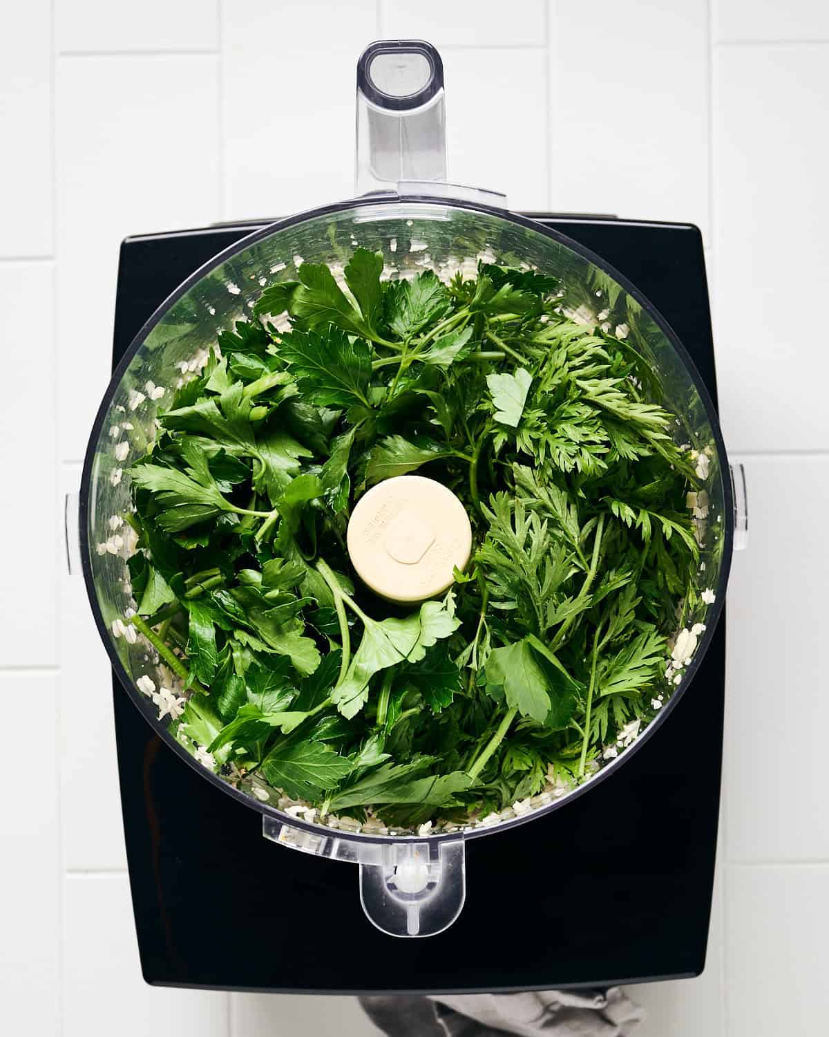 Coarsely chopped carrot tops and parsley added to food processor bowl.