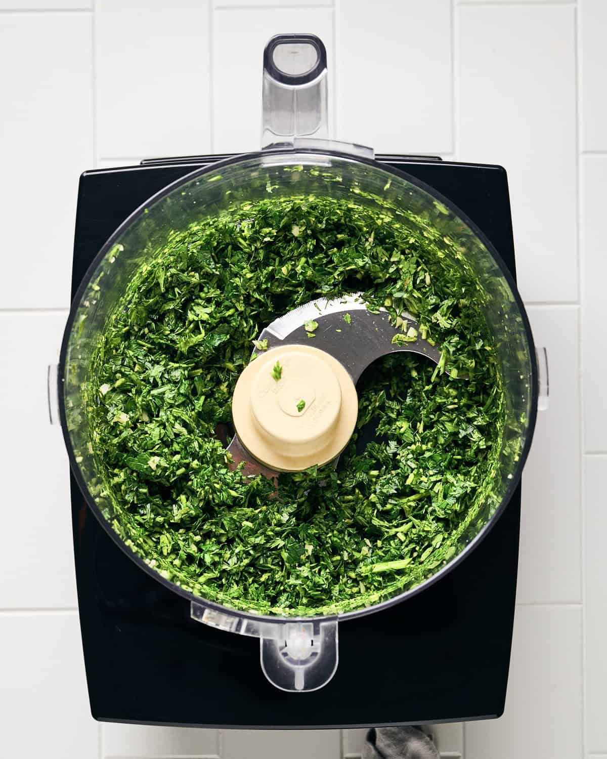 Chopped carrot tops, parsley, and garlic in a food processor bowl.