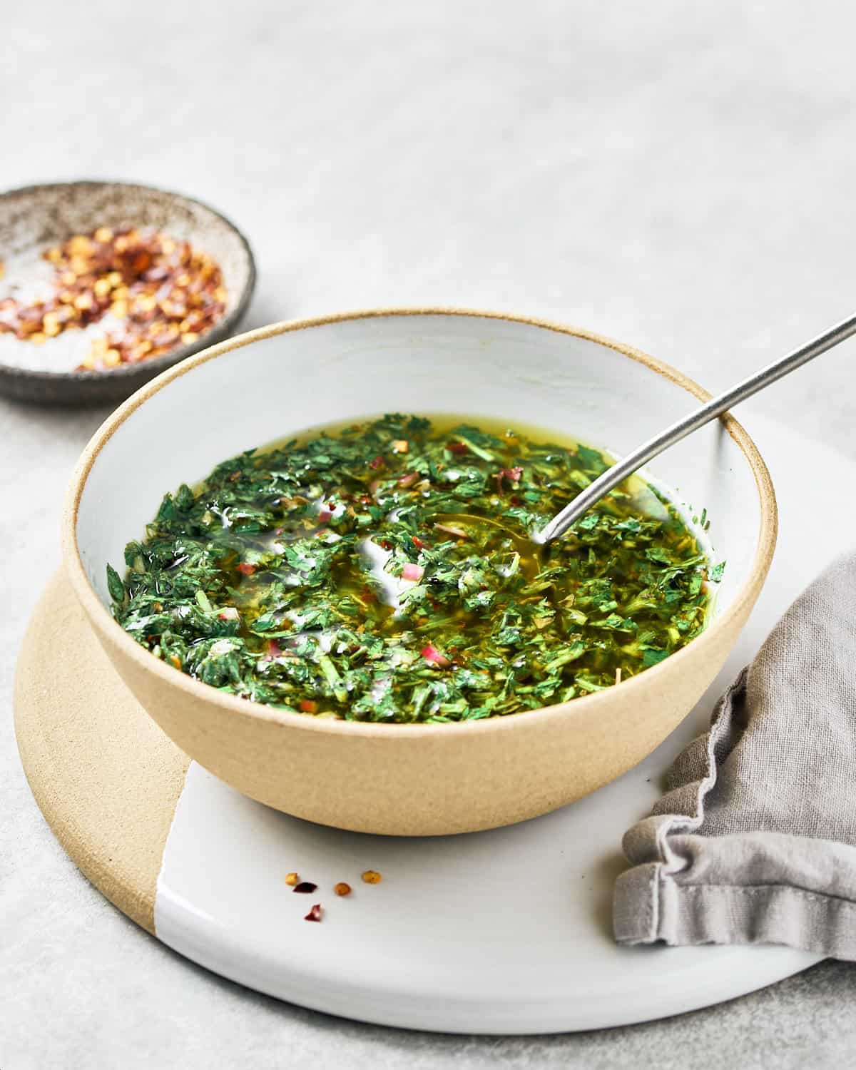 Bowl of carrot top chimichurri with a spoon and red pepper flakes.