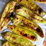 Several broiled Hatch chiles on aluminum foil on a baking sheet.