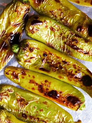 Several broiled Hatch chiles on aluminum foil on a baking sheet.