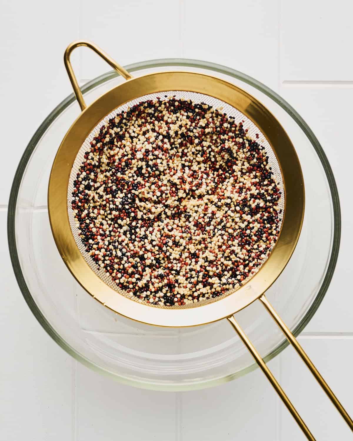 Rinsing quinoa in a sieve over a glass bowl.