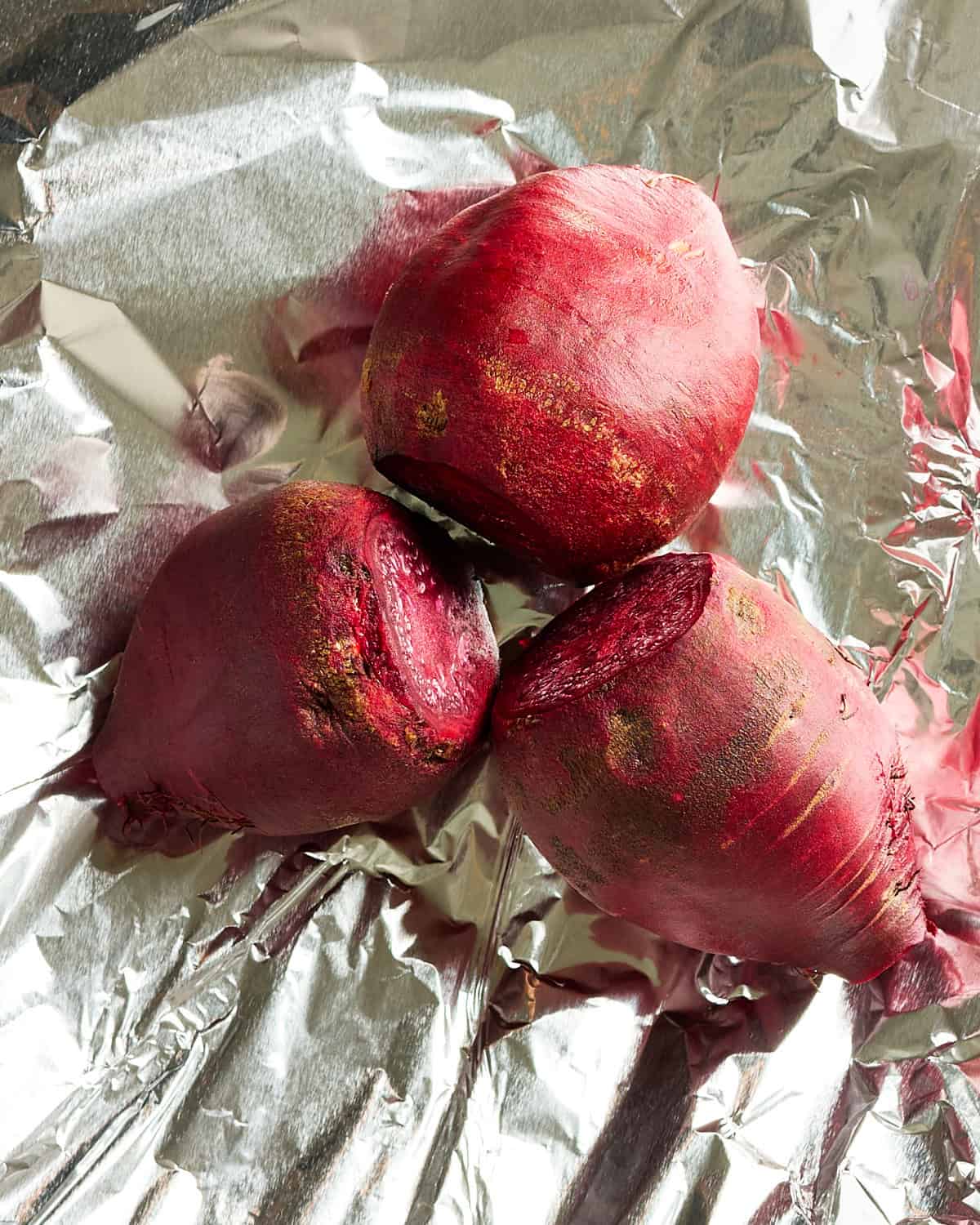 Three prepared beets placed on foil for roasting.