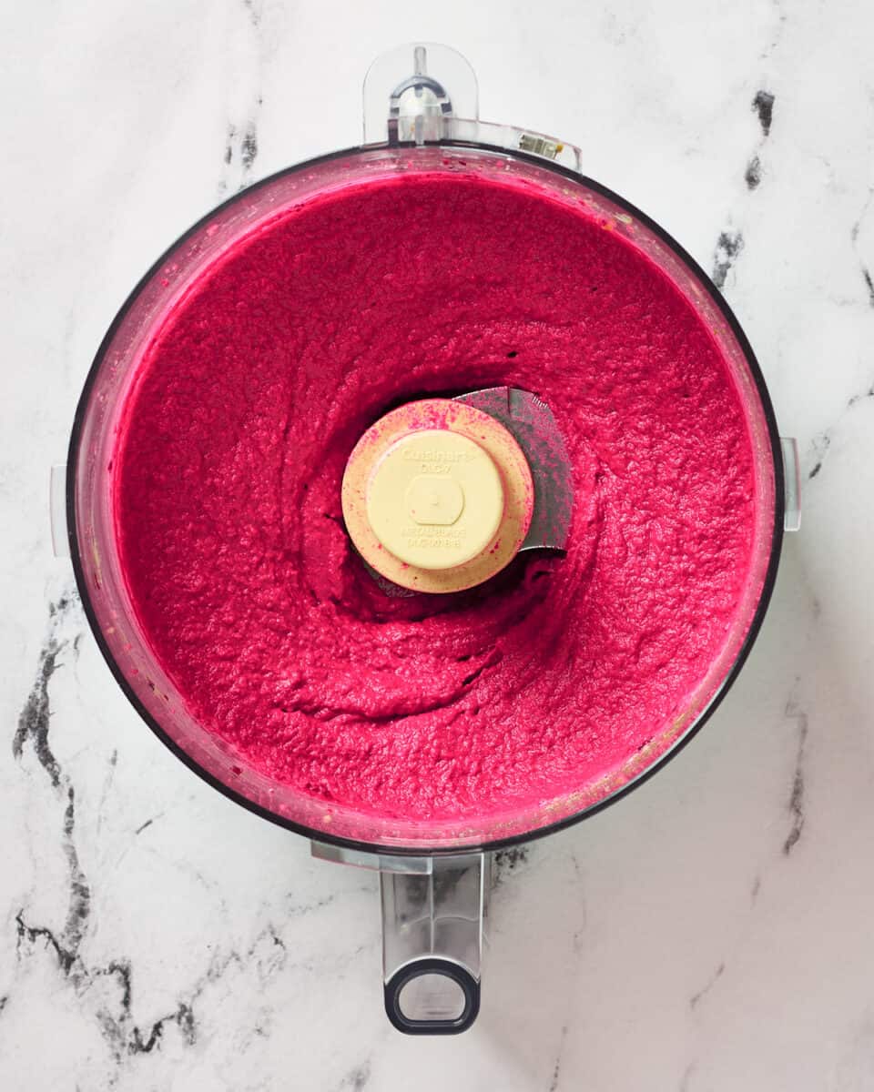 Creamy roasted beet hummus in a food processor bowl.