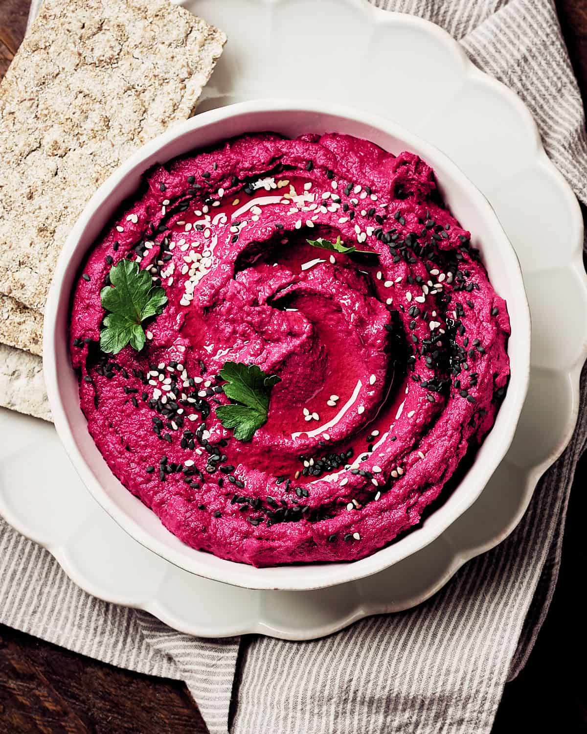 A bowl of beet hummus in a bowl with crackers on a plate.