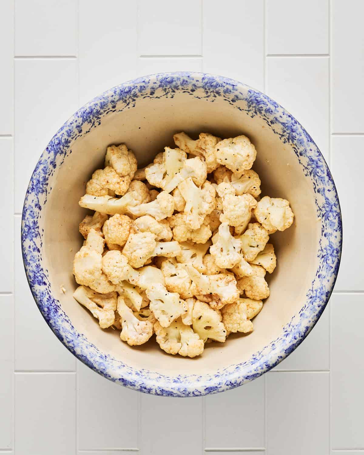 Fresh cauliflower florets tossed with spice mixture in a large bowl.