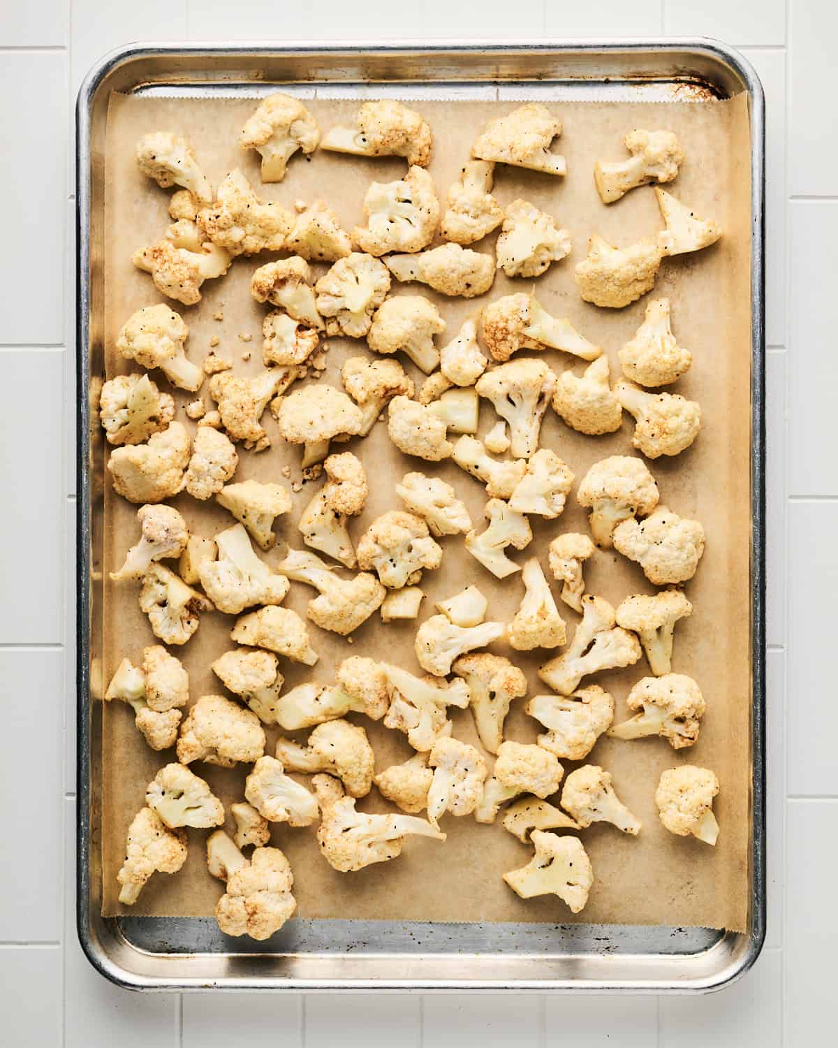 Raw cauliflower tossed with spices placed on a rimmed baking sheet.