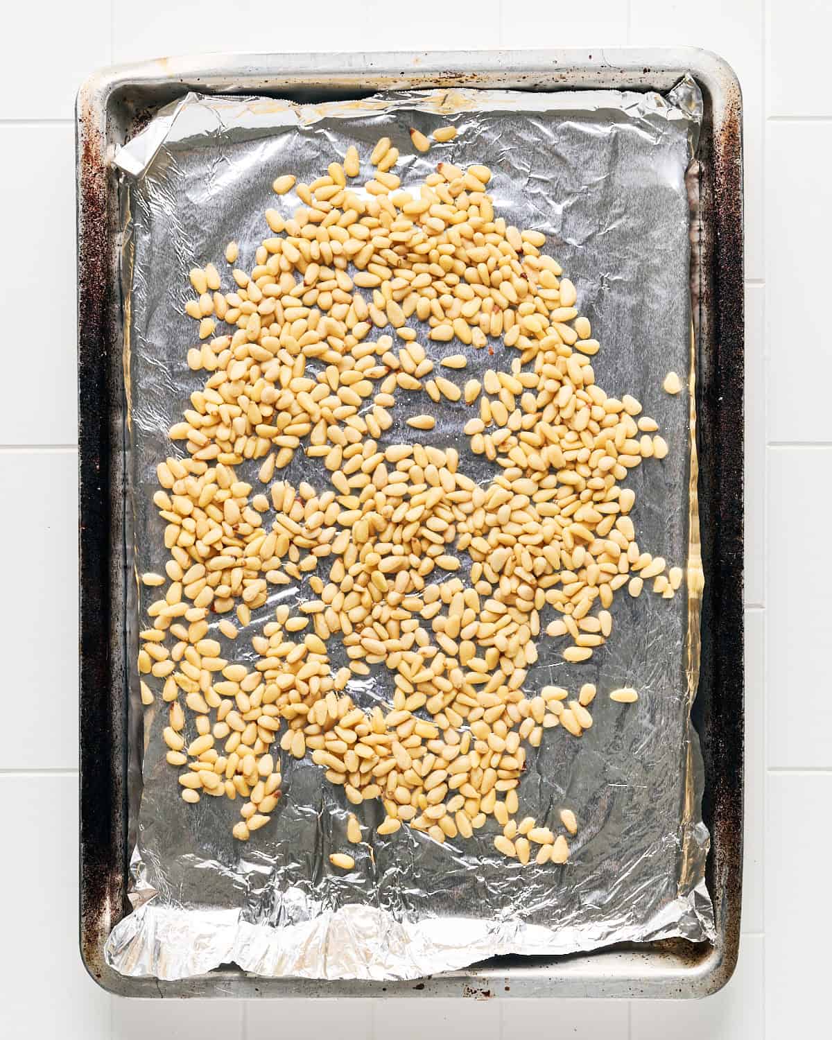 Baked pine nuts on aluminum foil on a baking sheet.