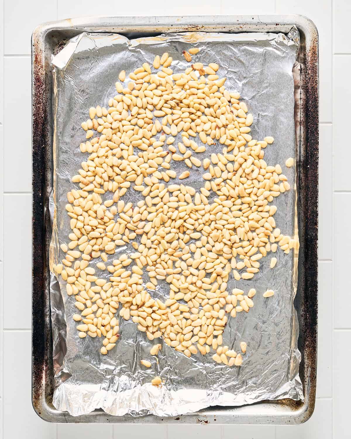 Raw pine nuts on a baking sheet with aluminum foil.