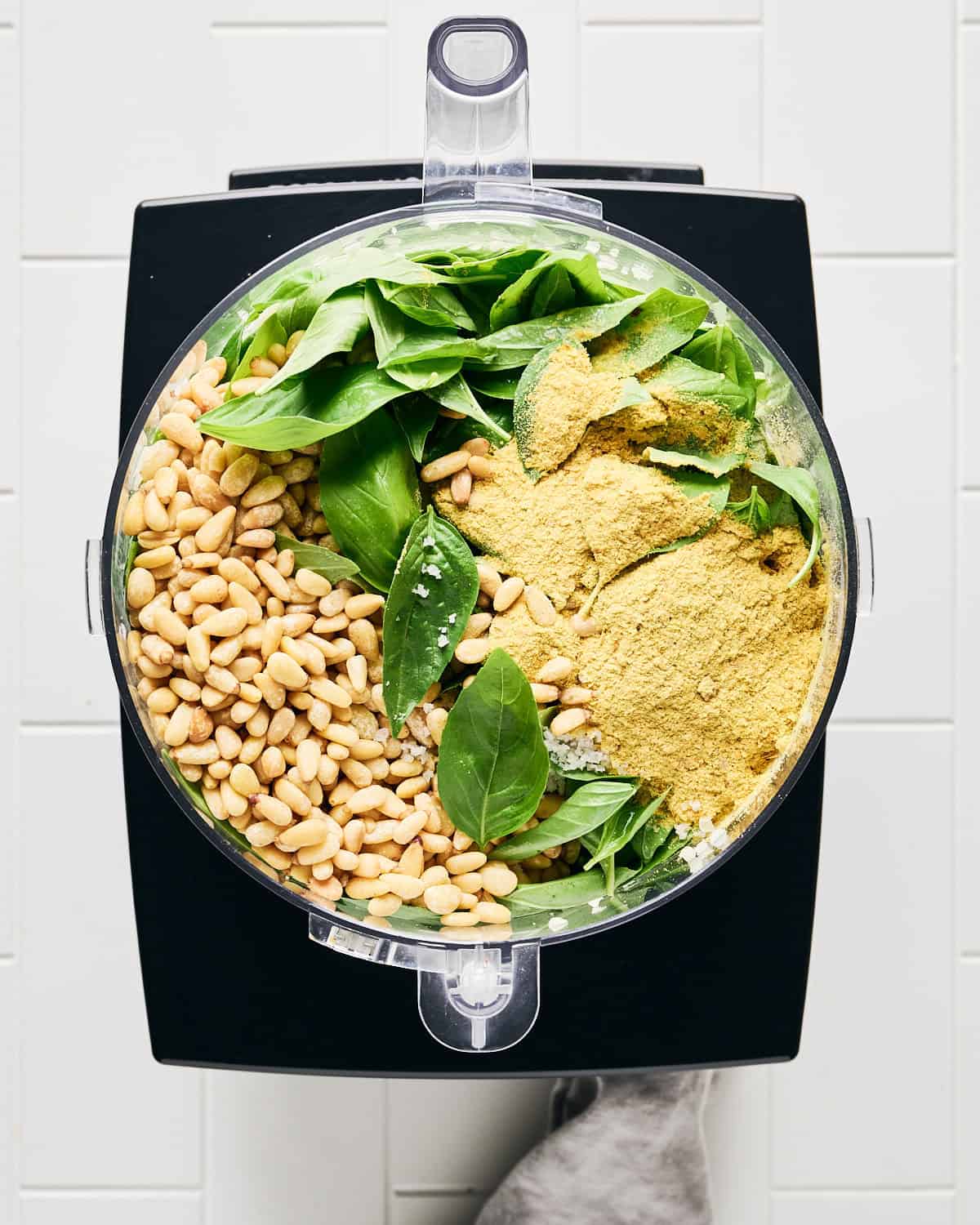 Ingredients added to food processor bowl except olive oil to make vegan basil pesto.