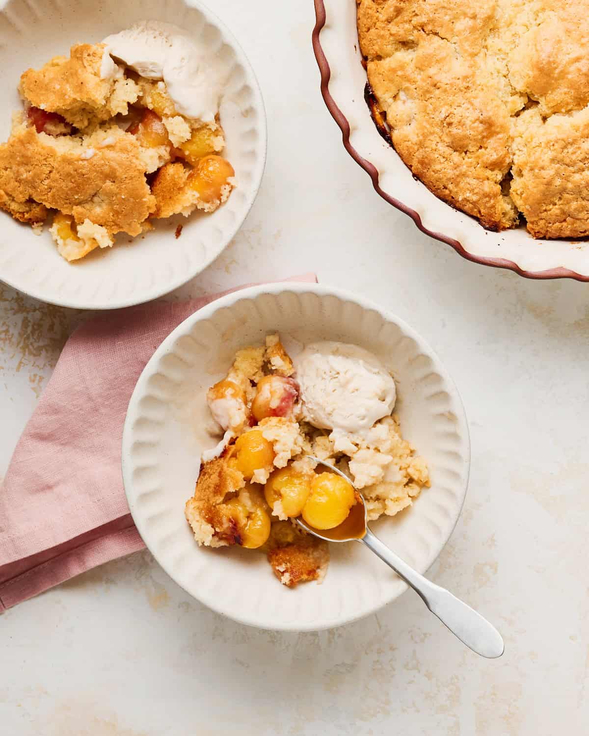 Vegan Cherry Cobbler with Rainier Cherries served with vegan vanilla ice cream in two bowls with the pie dish and a napkin.