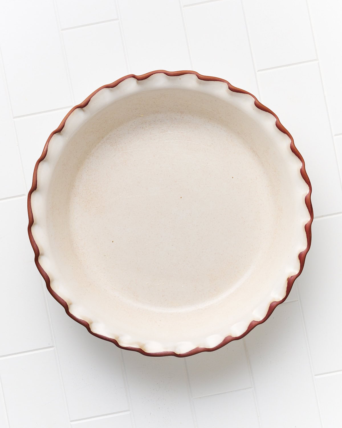 Buttered pie dish on a tile surface in preparation to make vegan cherry cobbler.