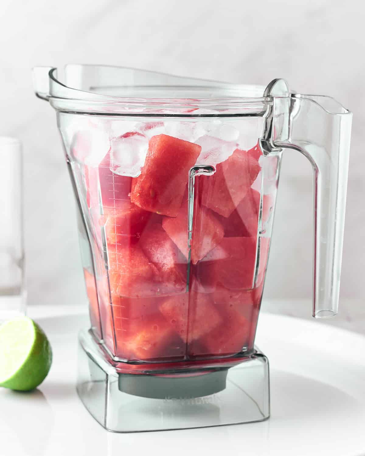 Chopped watermelon with ice and lemon juice in a plastic blender container.