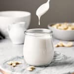 Spoon dripping cashew cream into a small glass jar.