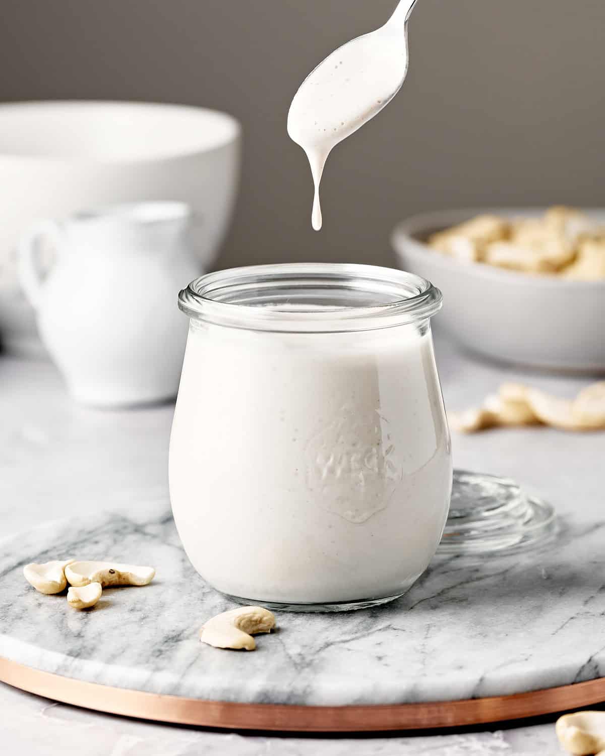Spoon dripping cashew cream into a small glass jar.