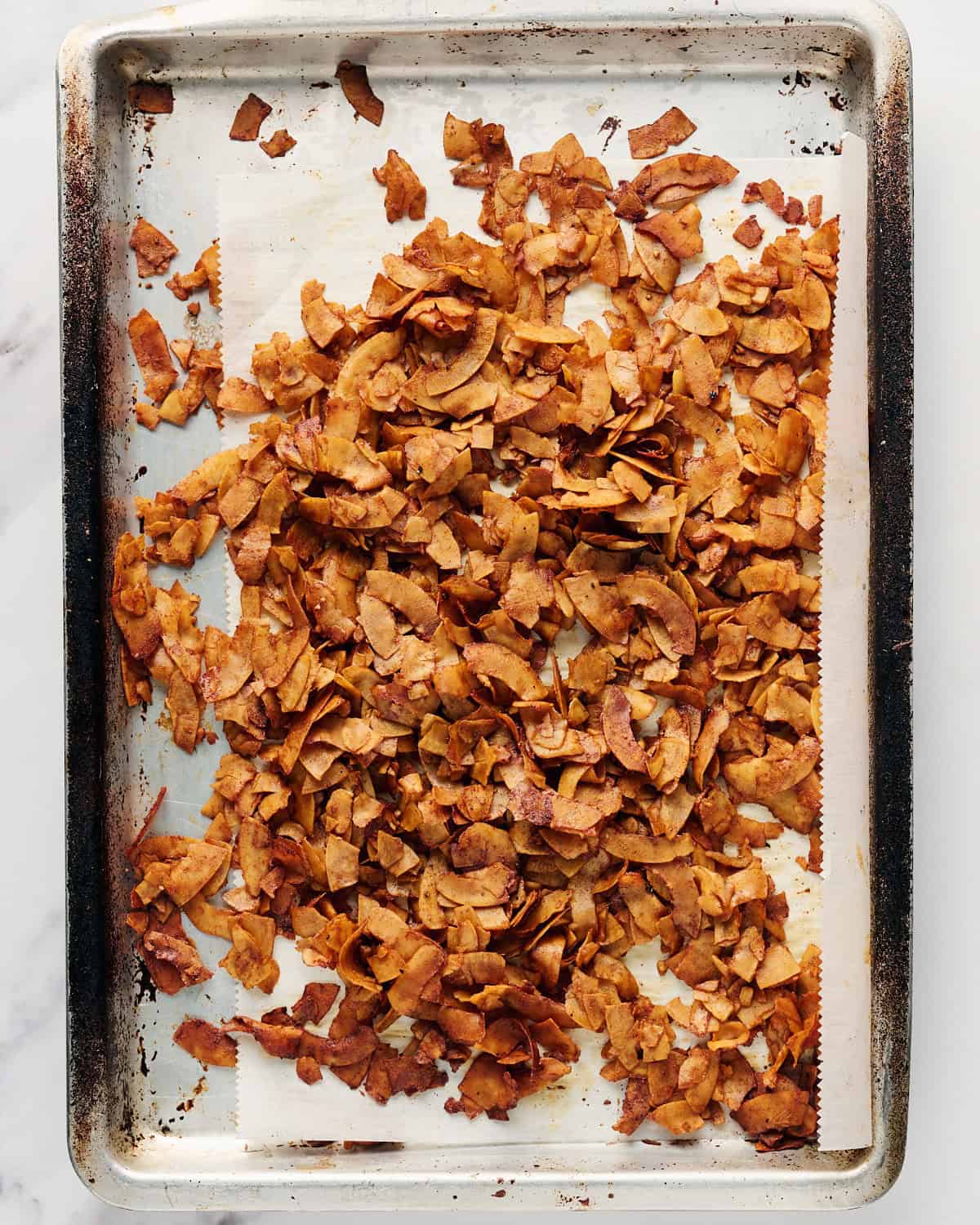 Baked coconut bacon on parchment paper on a rimmed baking sheet.