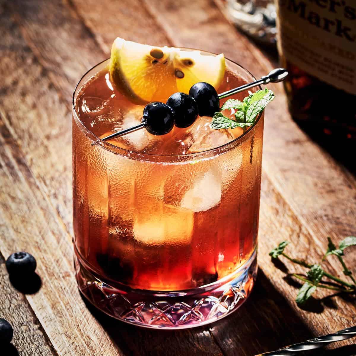 Blueberry Bourbon Smash with a mint garnish and cocktail stick of blueberries.