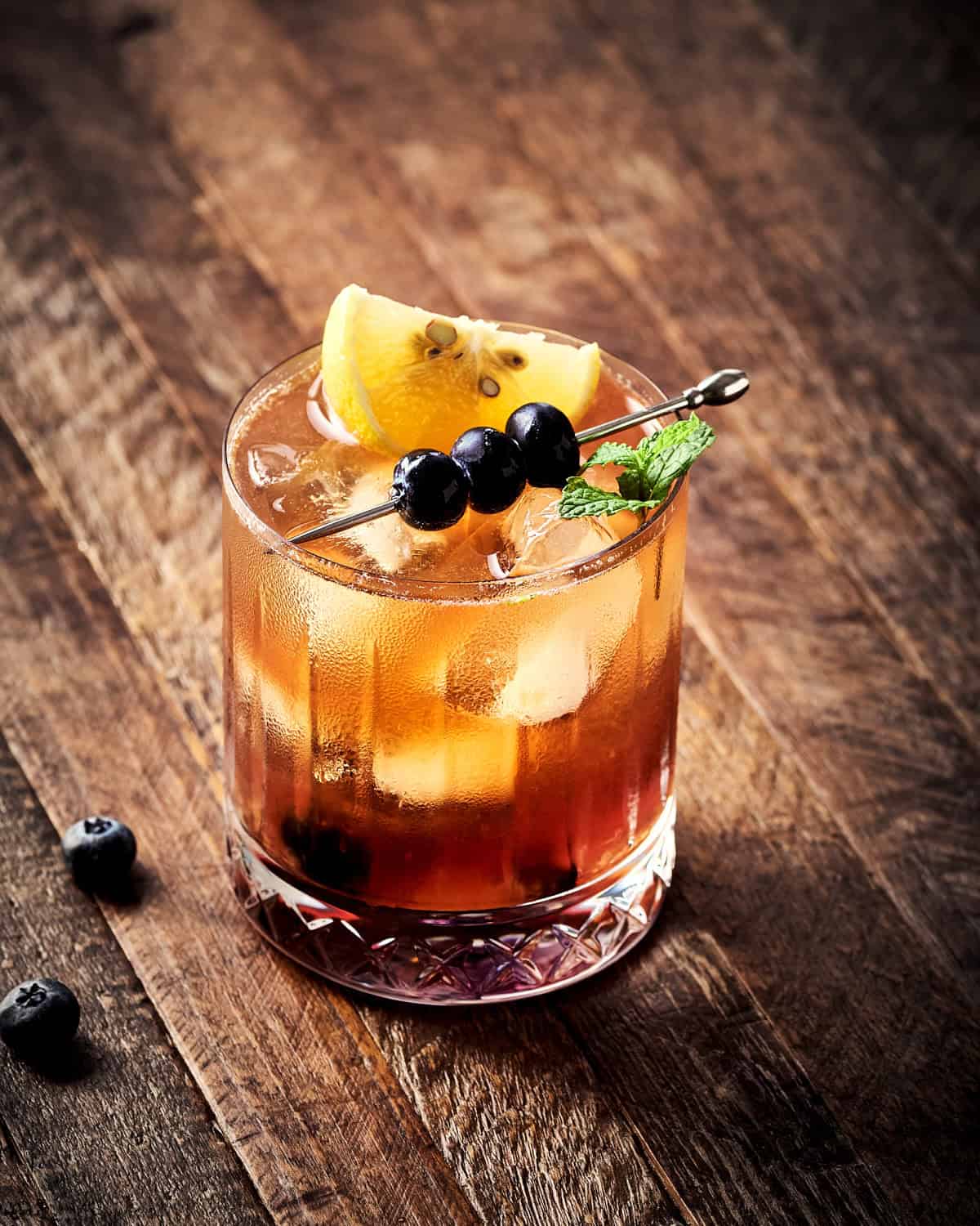 Blackberry Bourbon Smash garnished with lemon, mint, and blueberries.