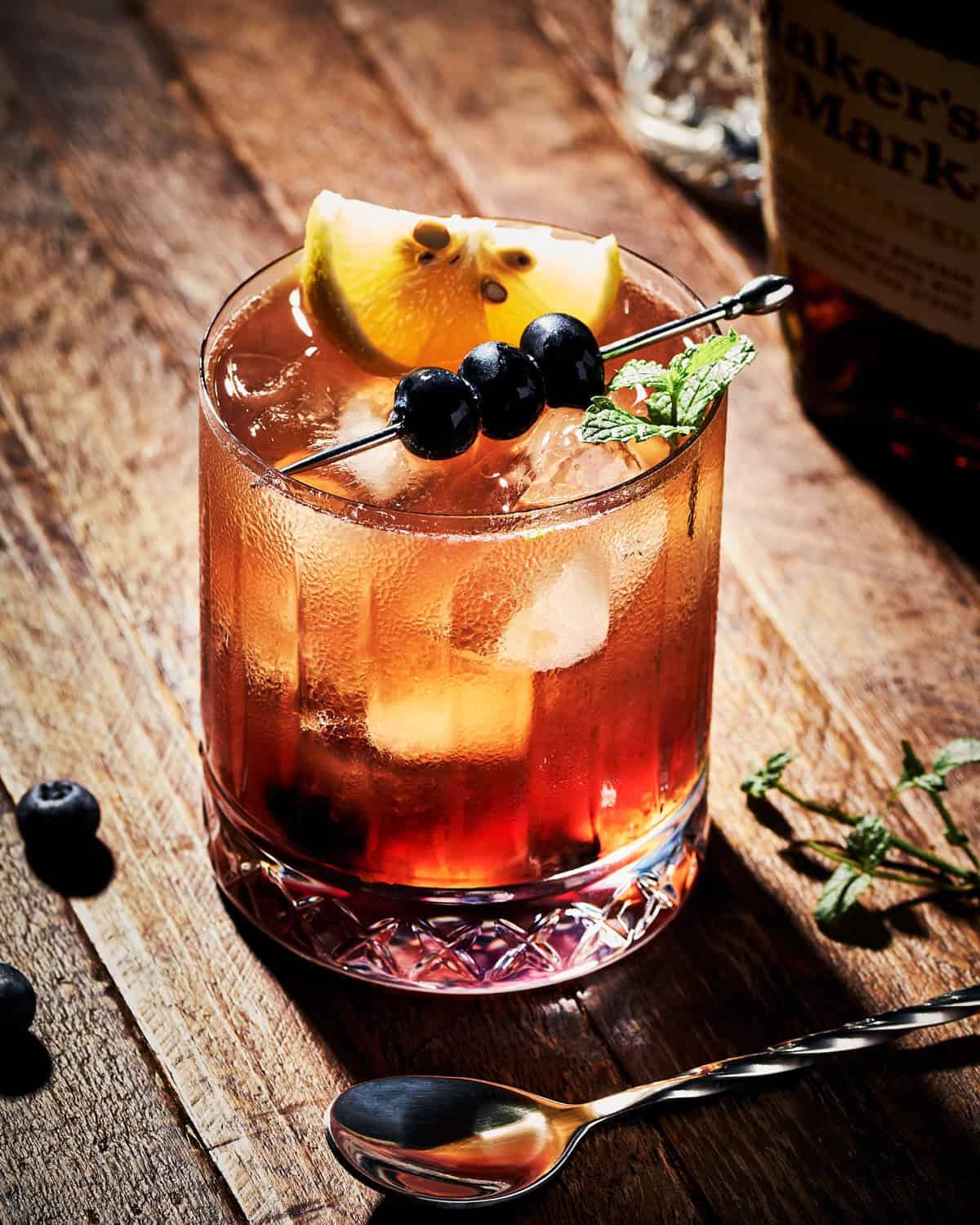 A cocktail glass of Blueberry Bourbon Smash garnish with lemon and mint.
