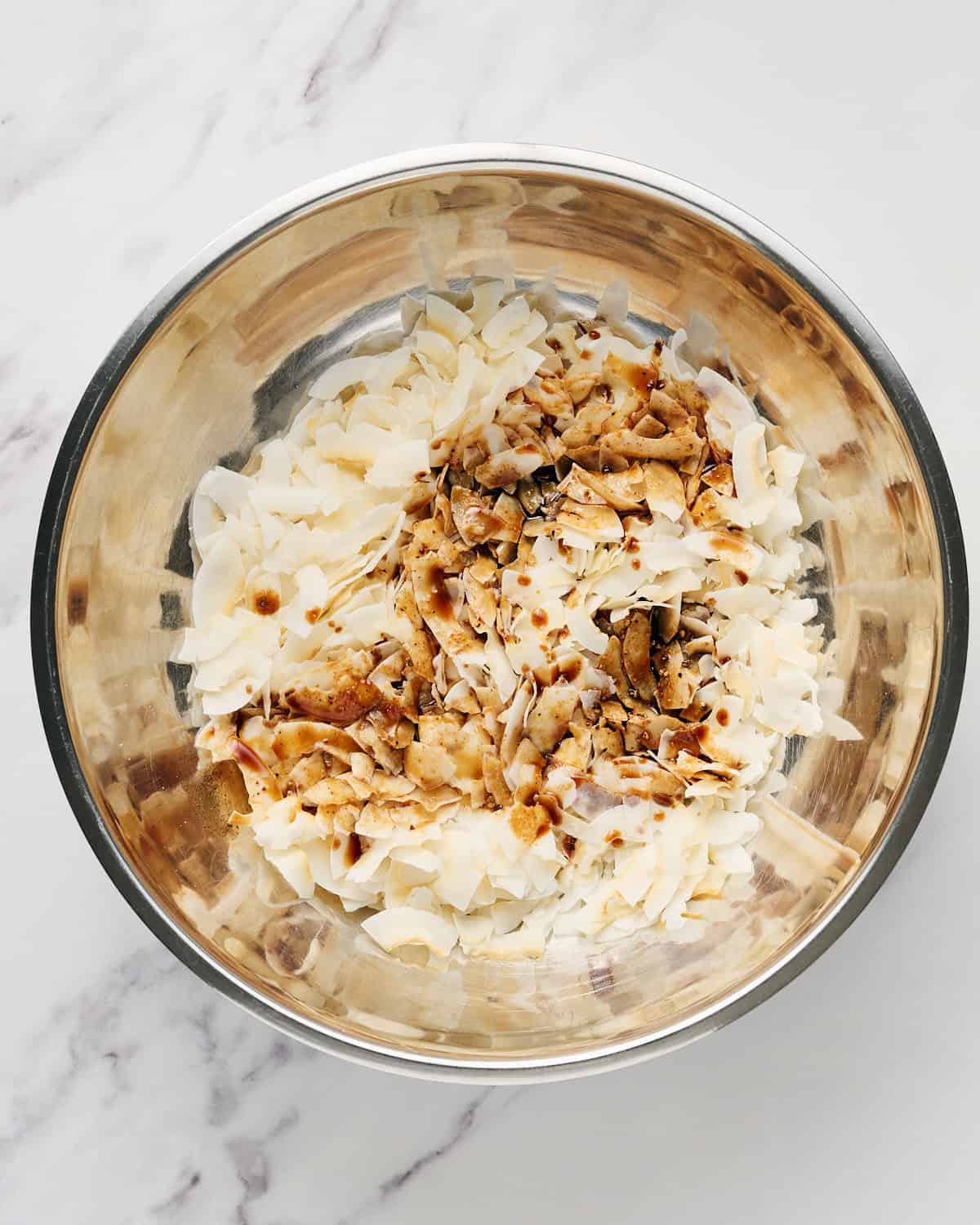Seasoning added to coconut flakes in a large bowl.