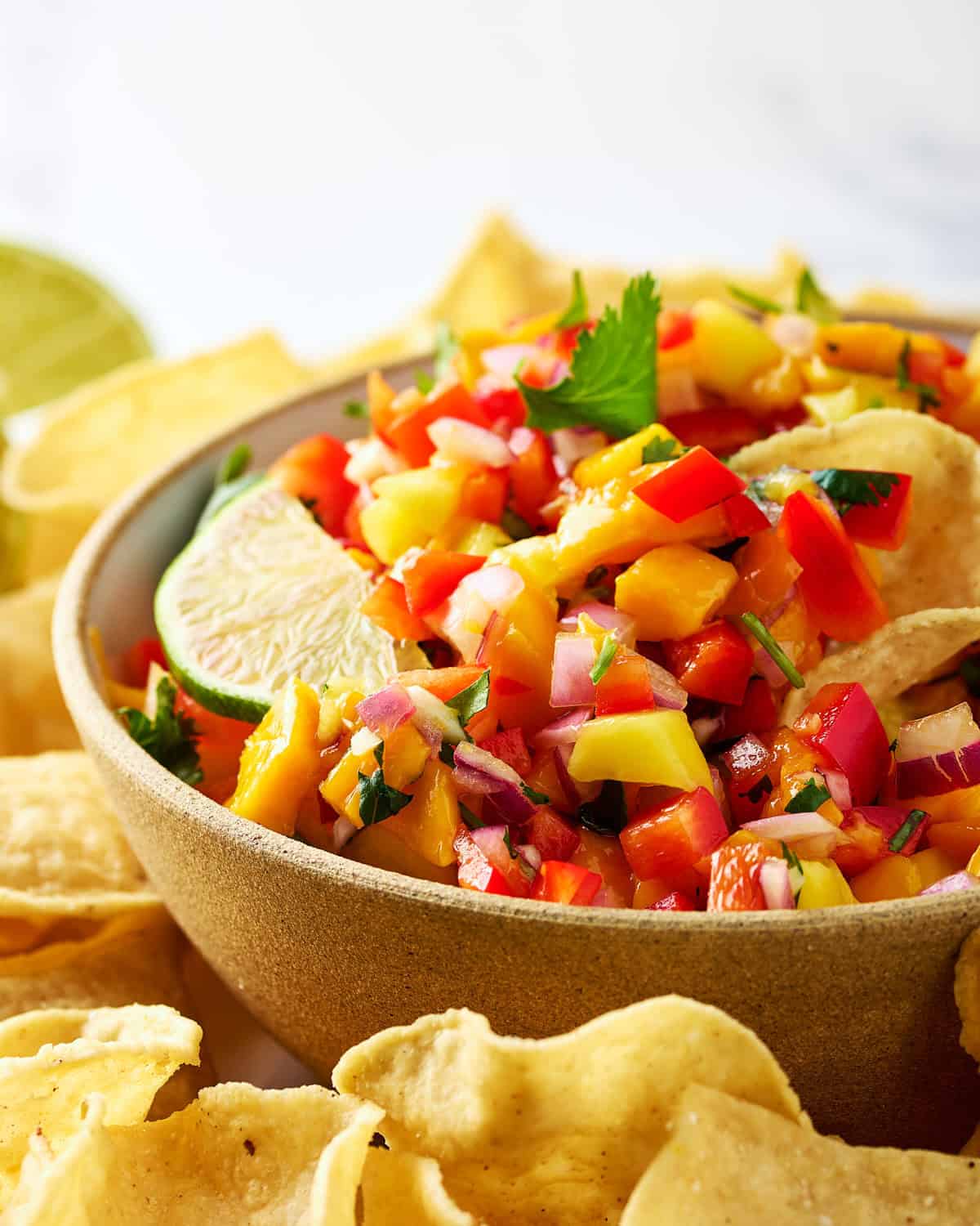Chopped fresh mango habanero salsa in a bowl next to tortilla chips and lime.
