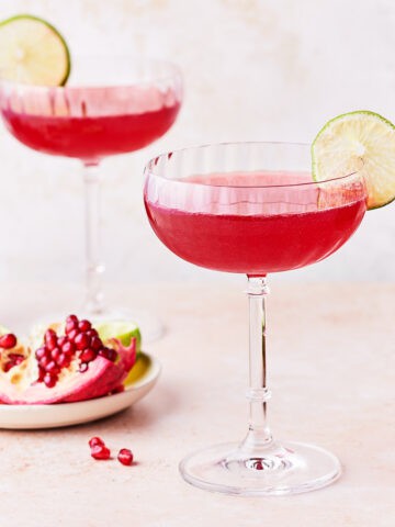Two coupe glasses filled with pomegranate gimlet.