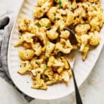 Platter of oven roasted cauliflower florets garnished with fresh parsley with spoon.