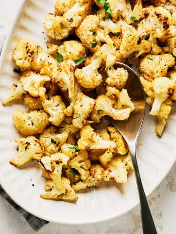 Platter of oven roasted cauliflower florets garnished with fresh parsley with spoon.