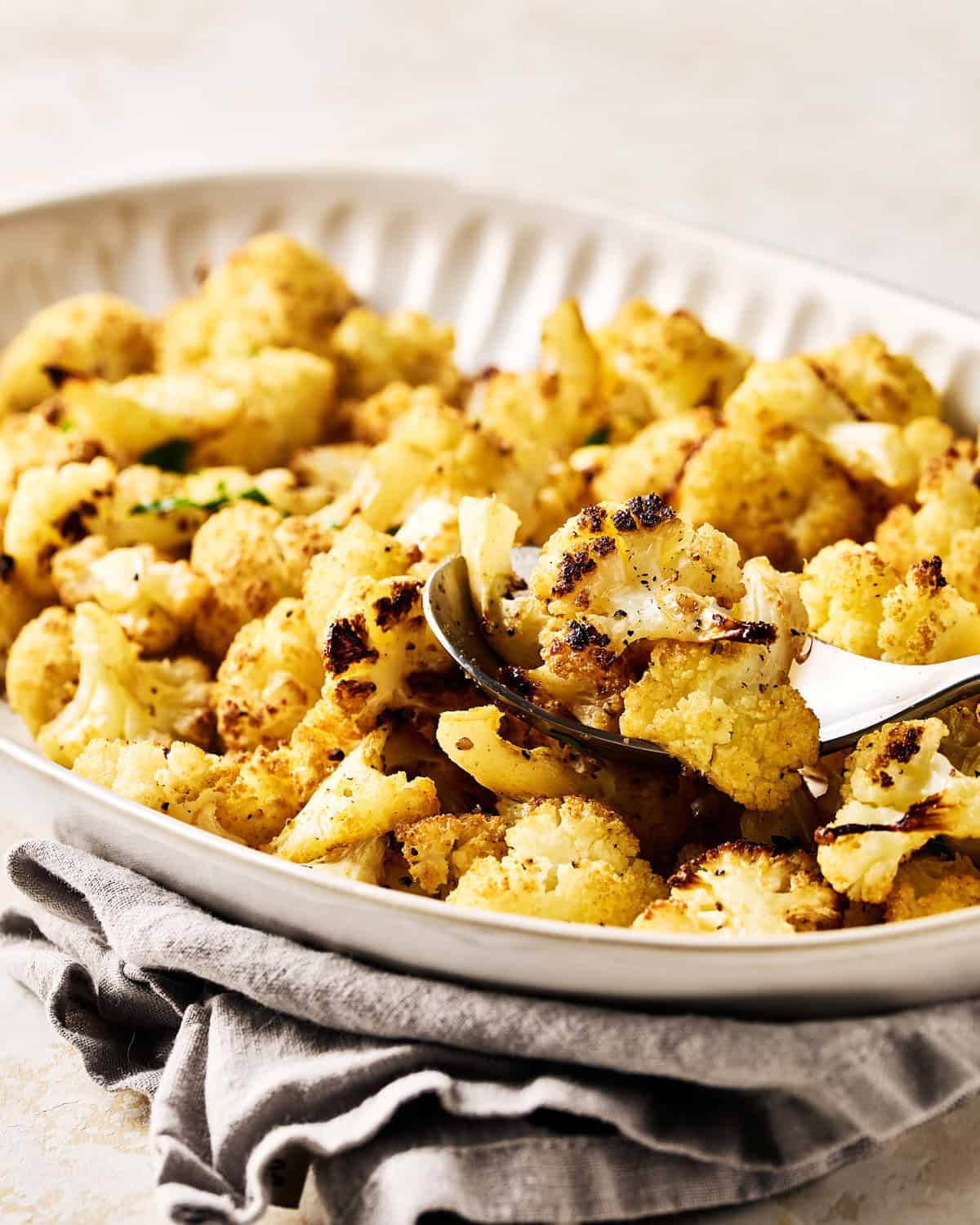 Platter of oven roasted cauliflower florets garnished with fresh parsley with spoon.