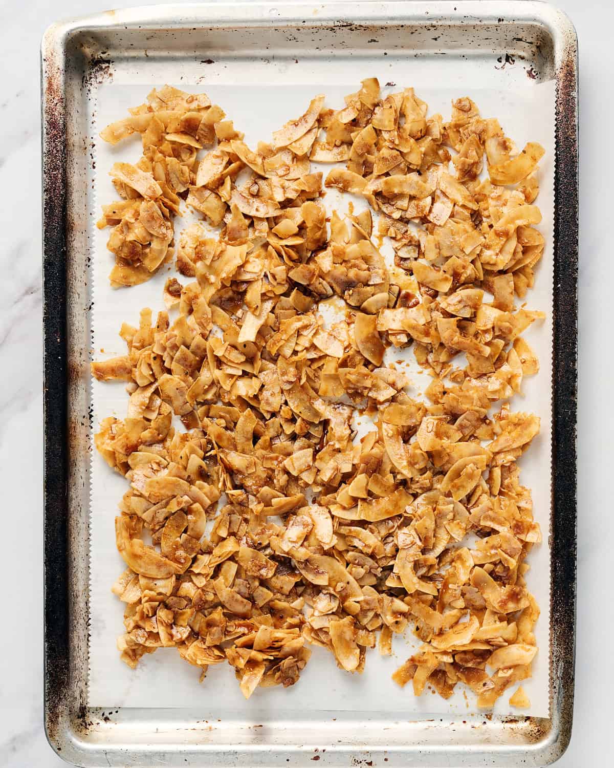 Unbaked coconut bacon on parchment paper on a rimmed baking sheet.