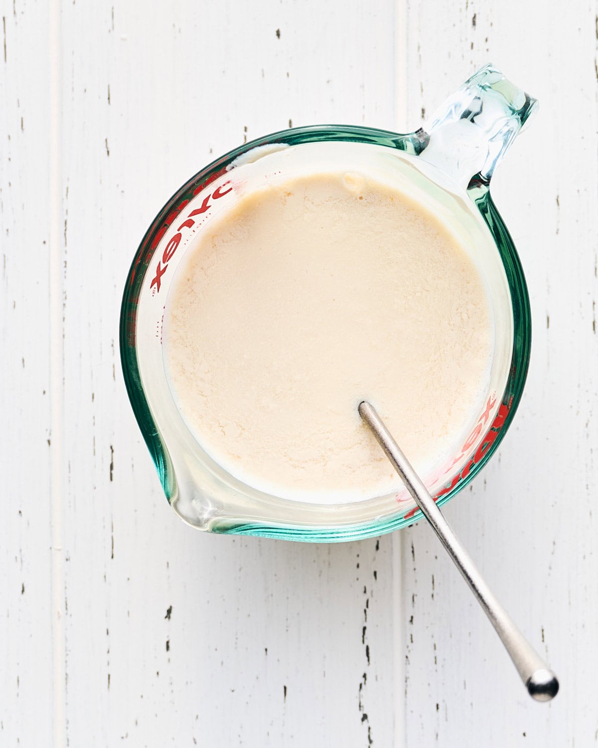 Vegan buttermilk in a glass measuring cup with a spoon.