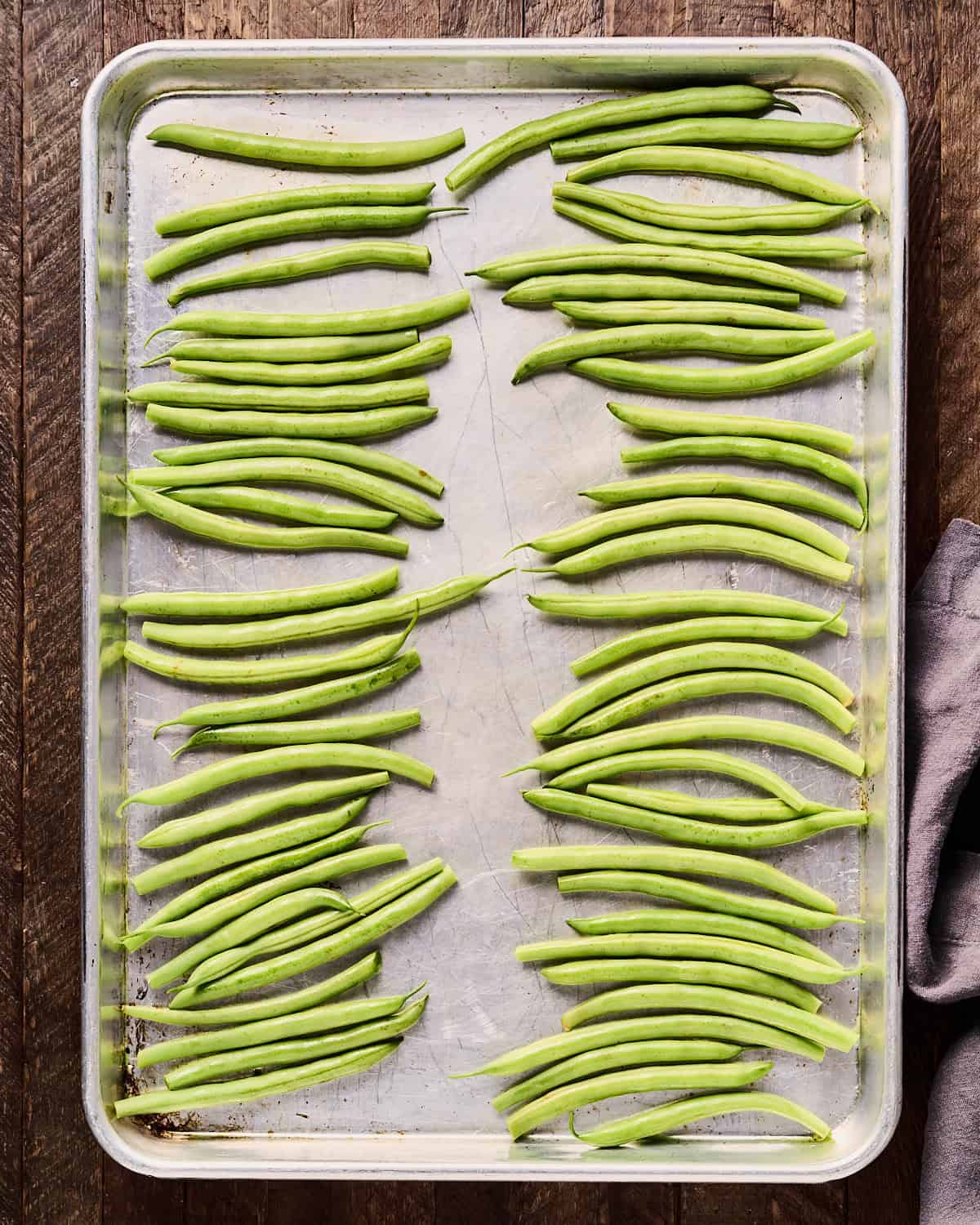 Green beans in two rows on a baking sheet rubbed with olive oil.