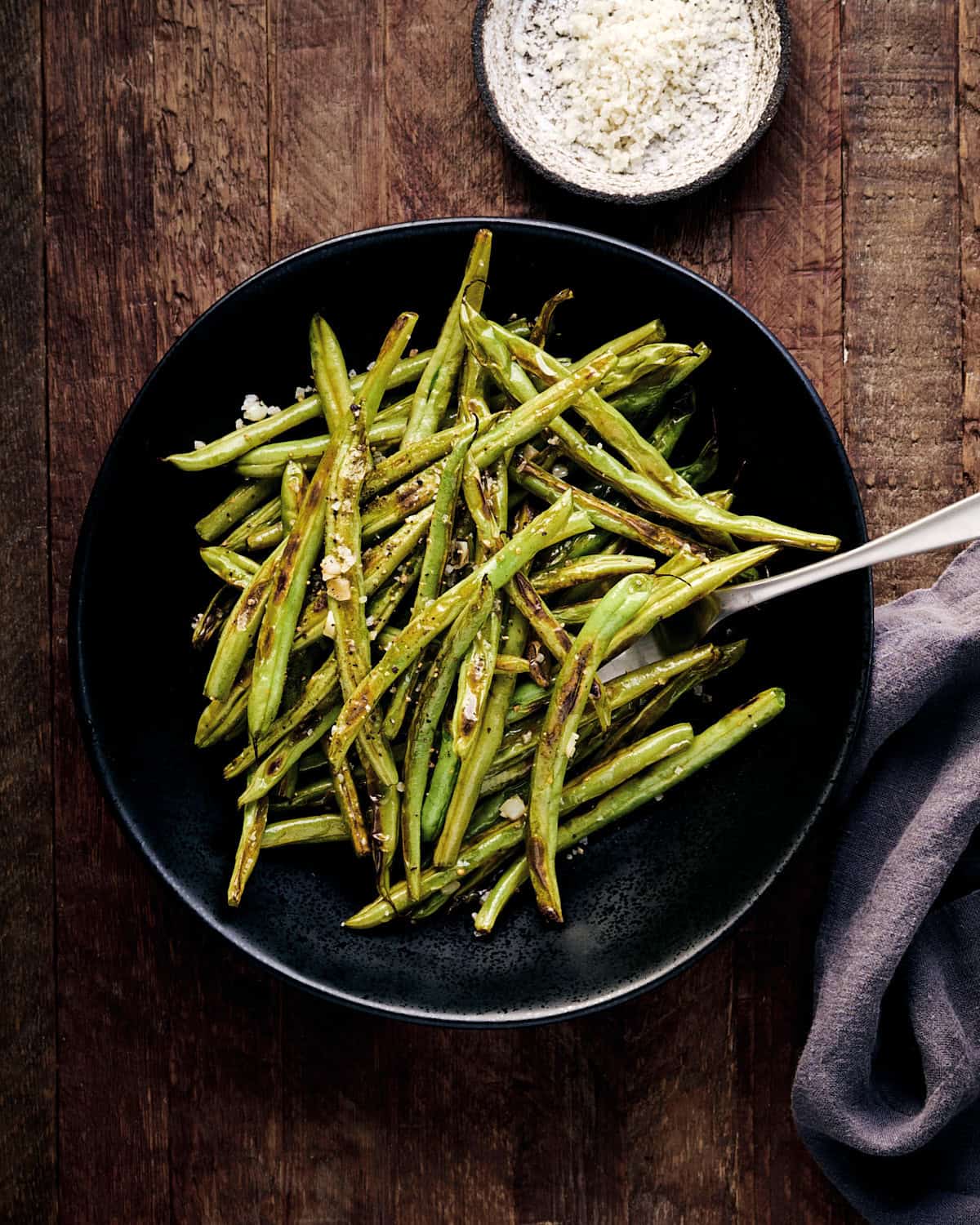 Roasted green beans with a serving fork and a napkin.