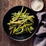Roasted green beans with garlic, salt, and pepper in a serving bowl.