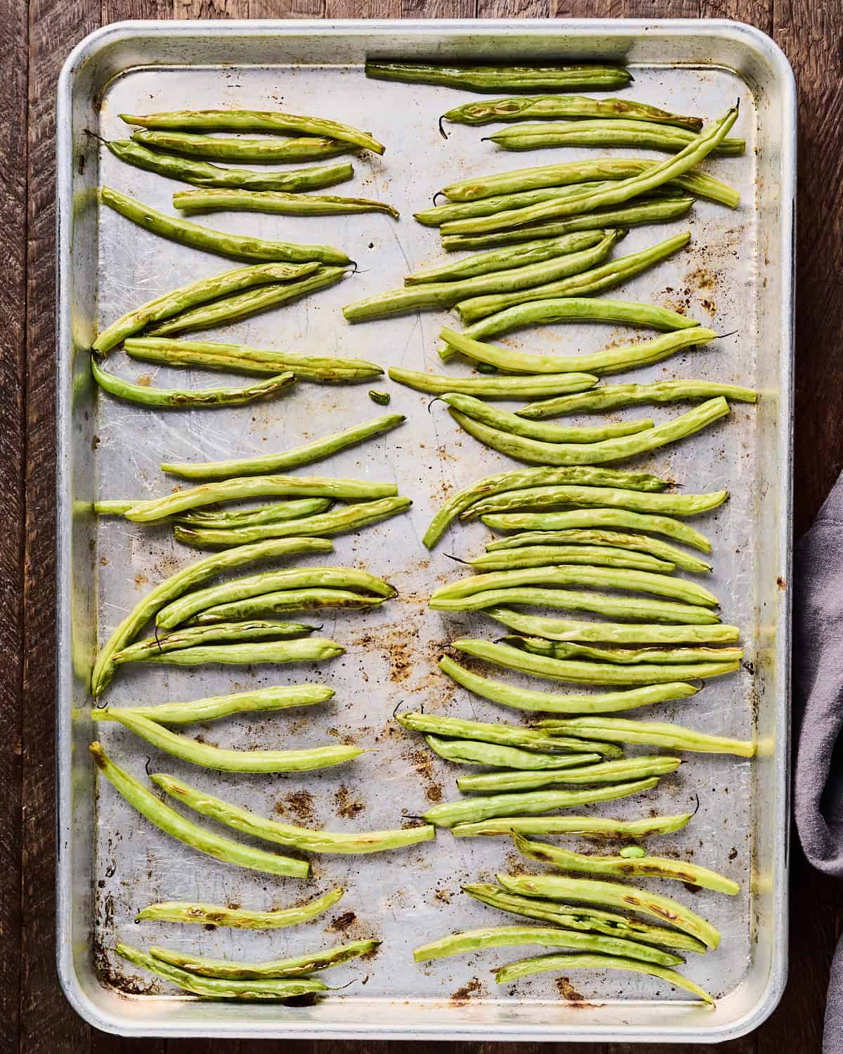 Partially roasted green beans with oil on a baking sheet.