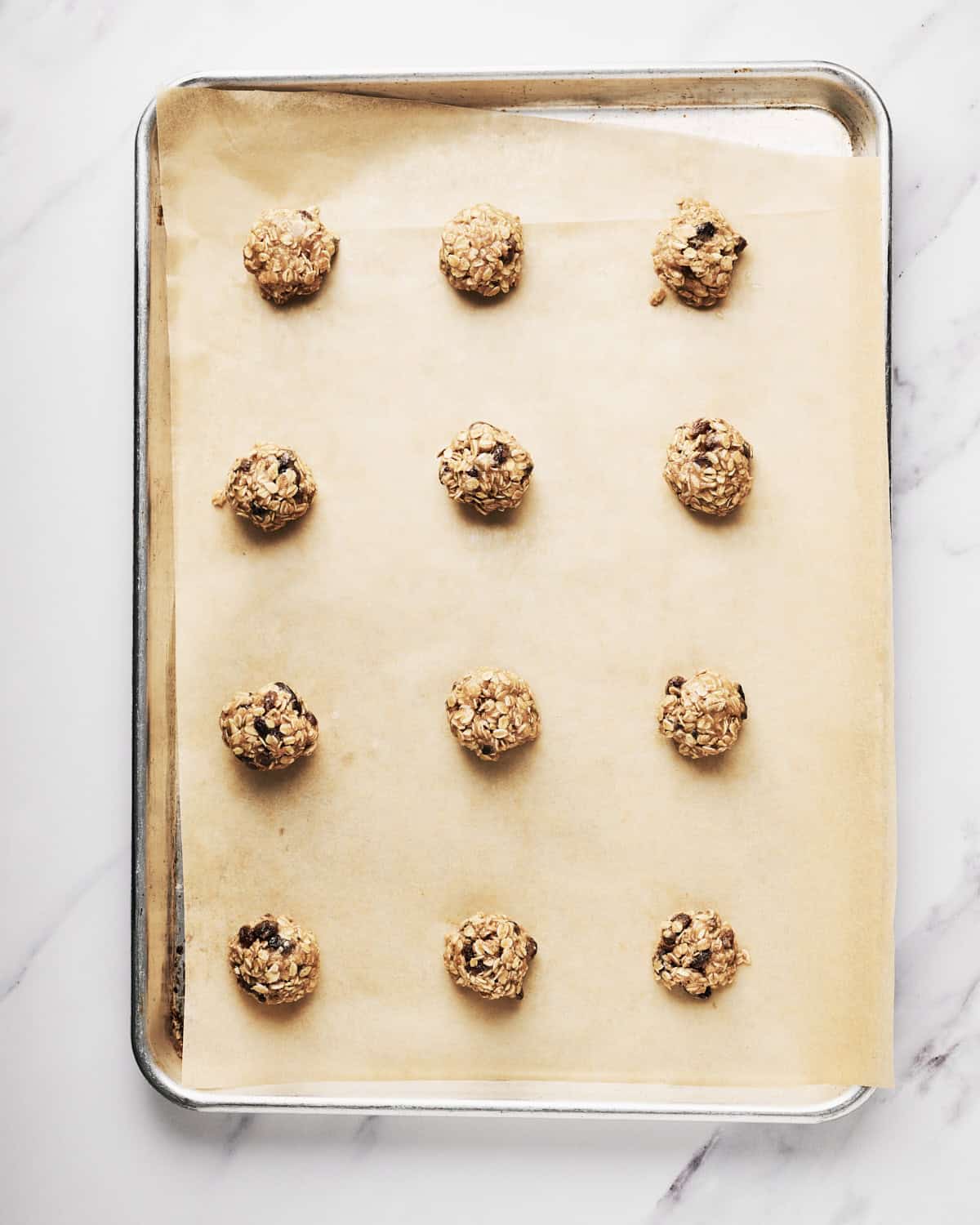 Unbaked vegan oatmeal raisin cookies on parchment paper on a cookie sheet.